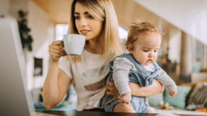 Image of a mother at a laptop holding a child, showing work life balance.